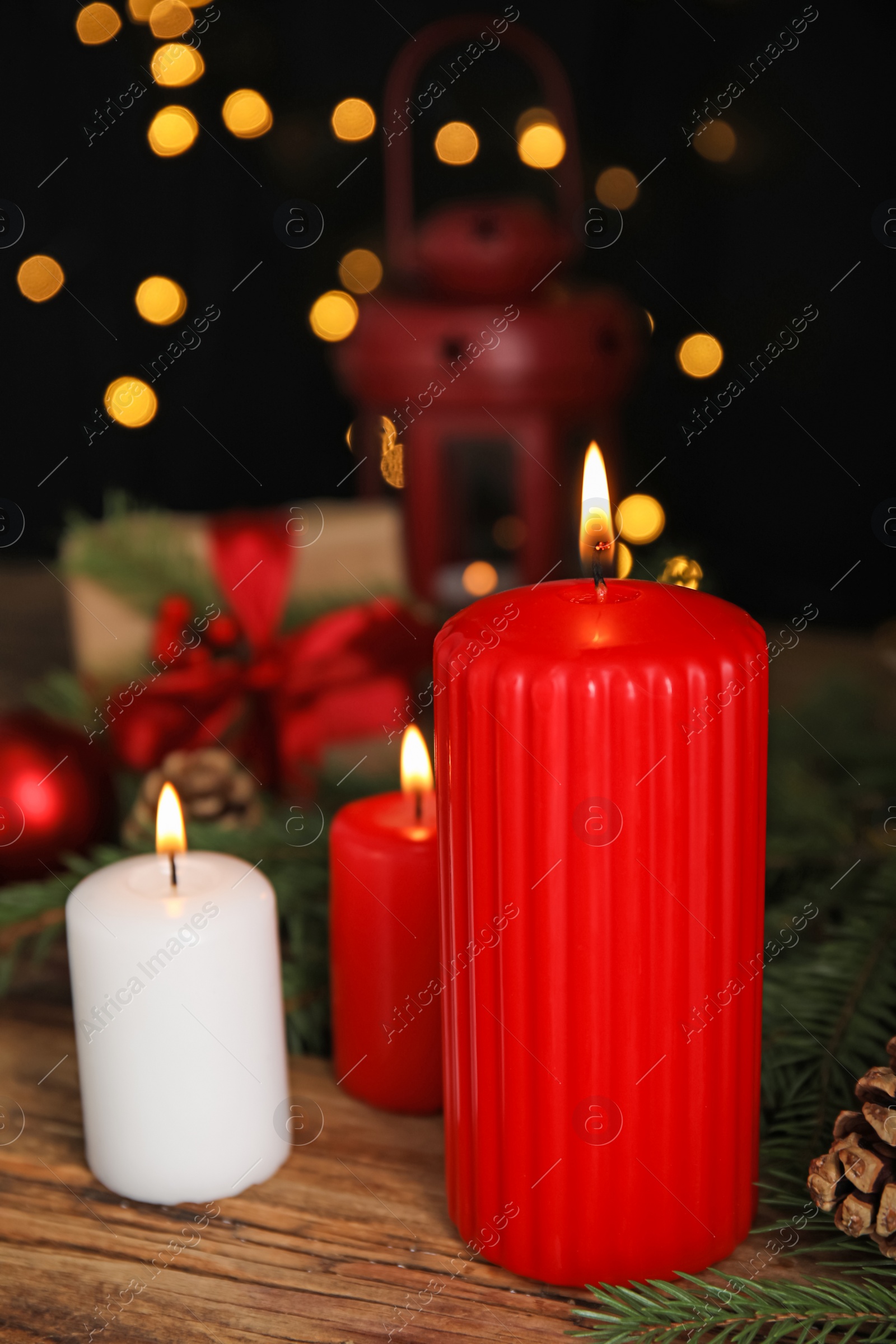 Photo of Burning candles and Christmas decor on wooden table against blurred festive lights