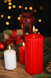 Photo of Burning candles and Christmas decor on wooden table against blurred festive lights