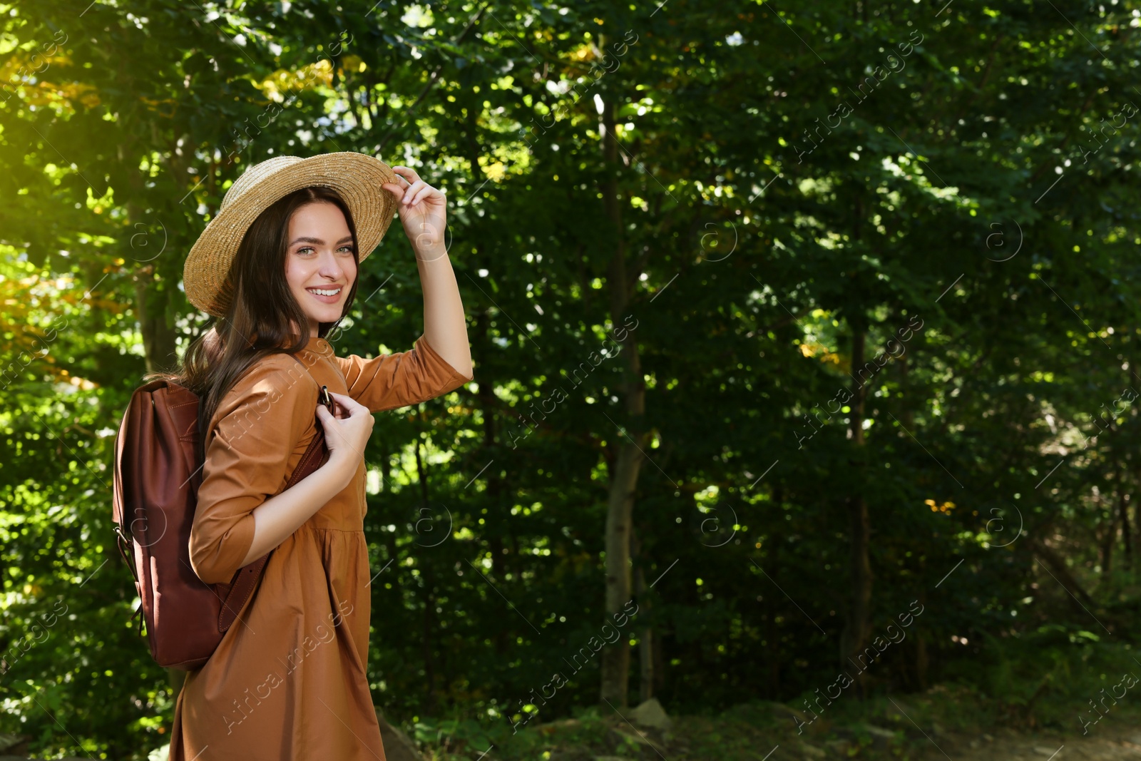 Photo of Happy woman with backpack and hat enjoying her walk in forest