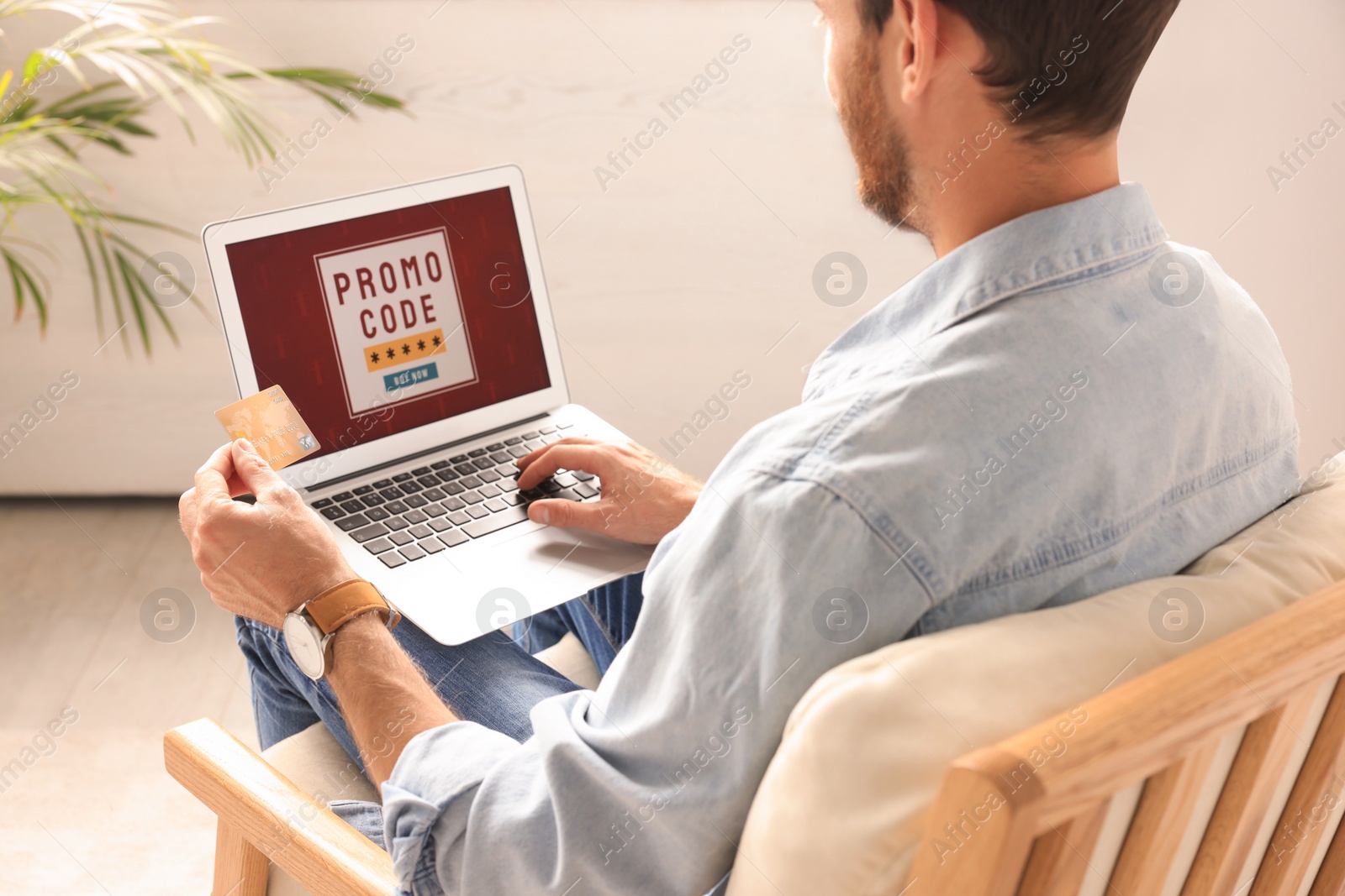 Photo of Man holding laptop with activated promo code and credit card indoors, closeup