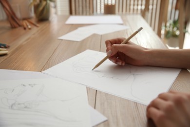 Photo of Young woman drawing male portrait at table indoors, closeup