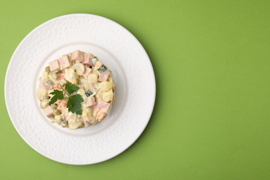 Photo of Tasty Olivier salad with boiled sausage on green table, top view. Space for text
