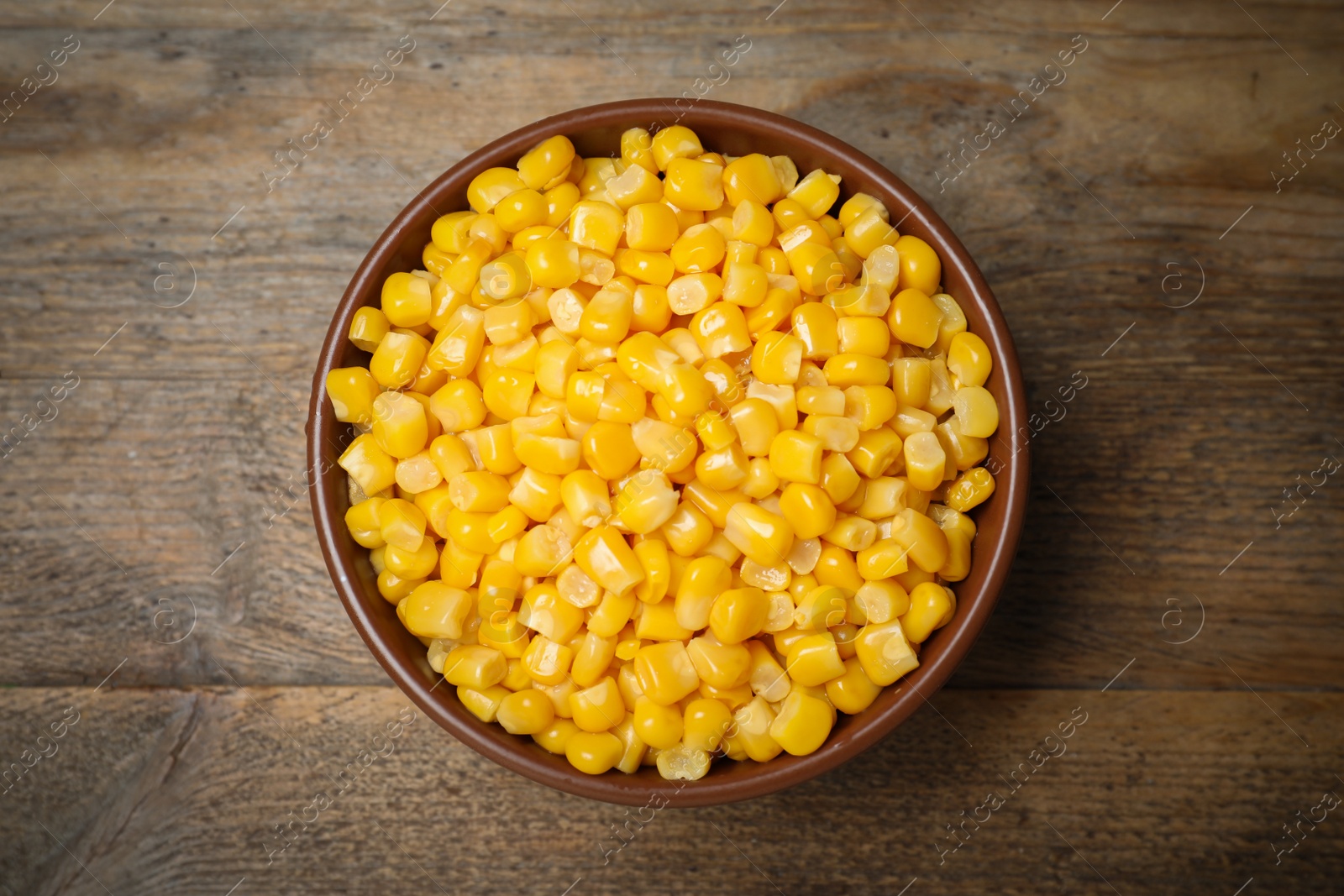 Photo of Delicious canned corn in bowl on wooden table, top view