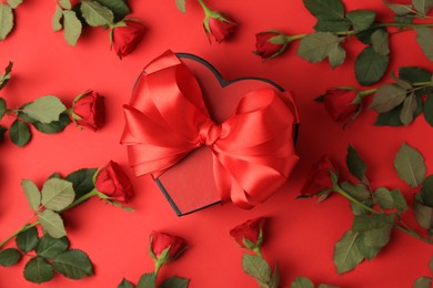 Photo of Heart shaped gift box with bow and beautiful roses on red background, flat lay