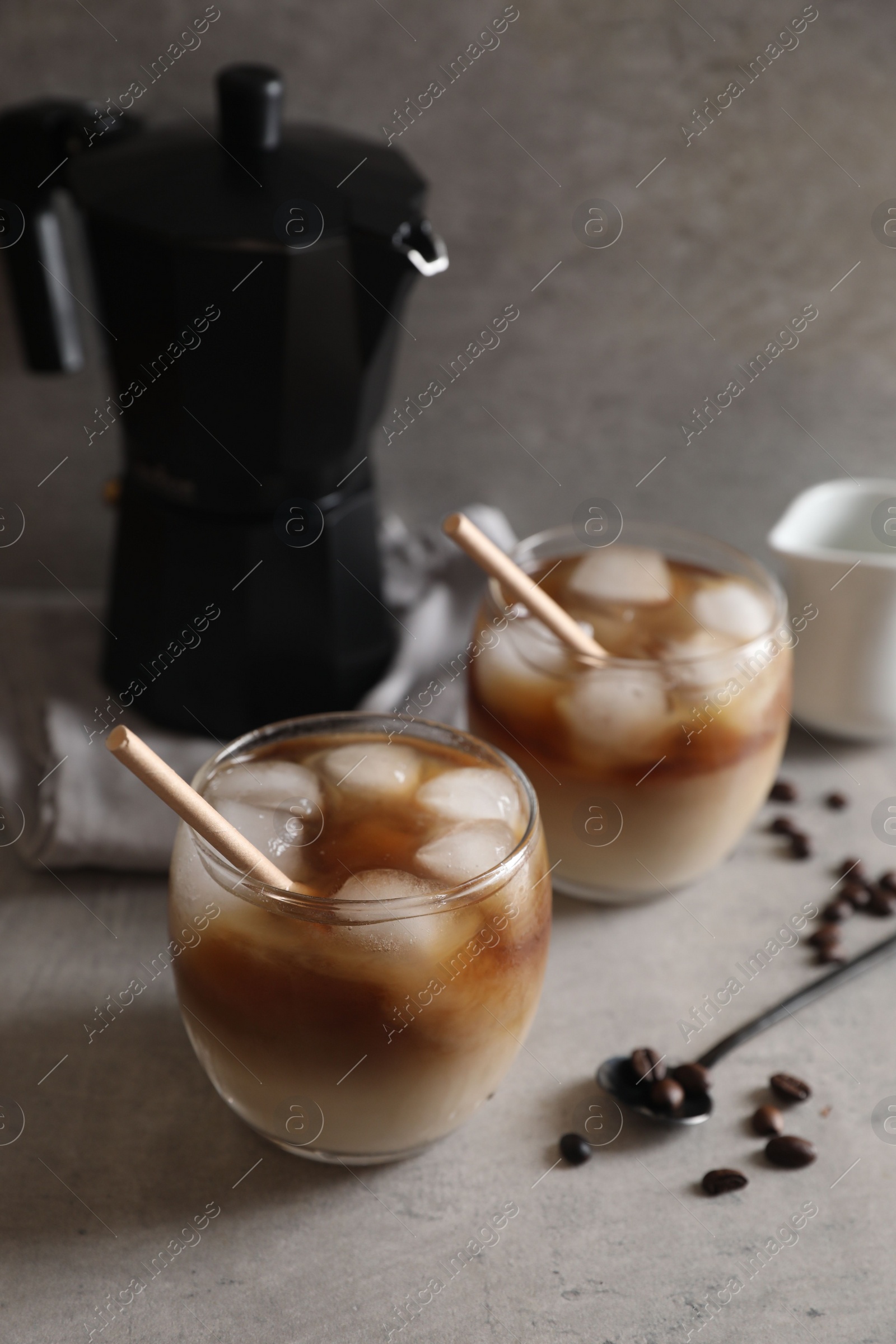 Photo of Refreshing iced coffee with milk in glasses, beans and spoon on gray table, closeup