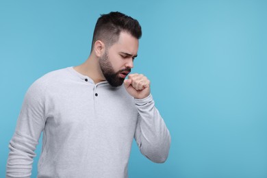 Sick man coughing on light blue background, space for text