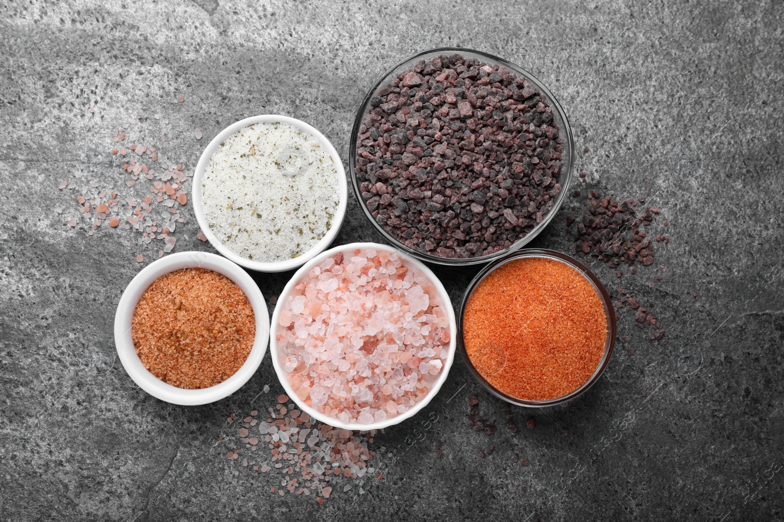 Photo of Different kinds of salt on grey table, flat lay