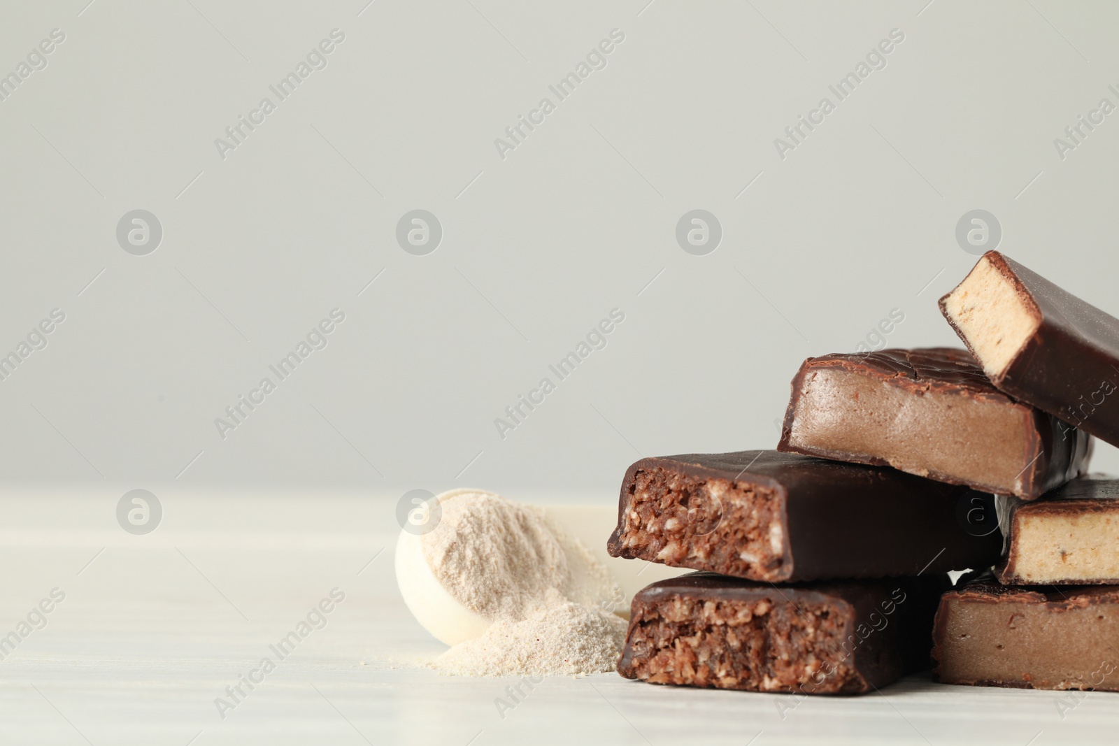 Photo of Pieces of tasty bars and spoon with protein powder on white table. Space for text