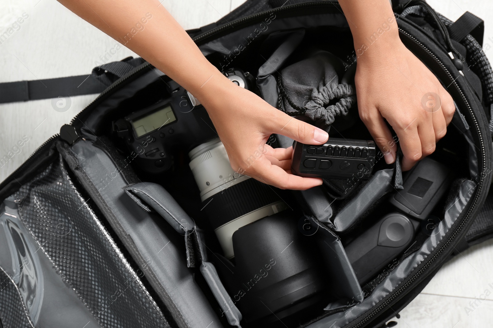 Photo of Woman putting professional photographer's equipment into backpack on floor, top view
