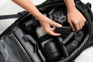 Woman putting professional photographer's equipment into backpack on floor, top view