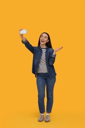 Smiling young woman taking selfie with smartphone on yellow background