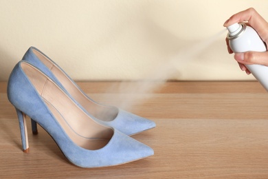 Image of Woman spraying deodorant over pair of shoes at home, closeup