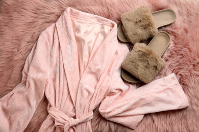 Photo of Pair of fluffy slippers and robe on fuzzy carpet, flat lay. Comfortable home outfit