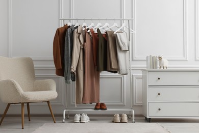Photo of Rack with different stylish women`s clothes, shoes, dresser and armchair near white wall in room