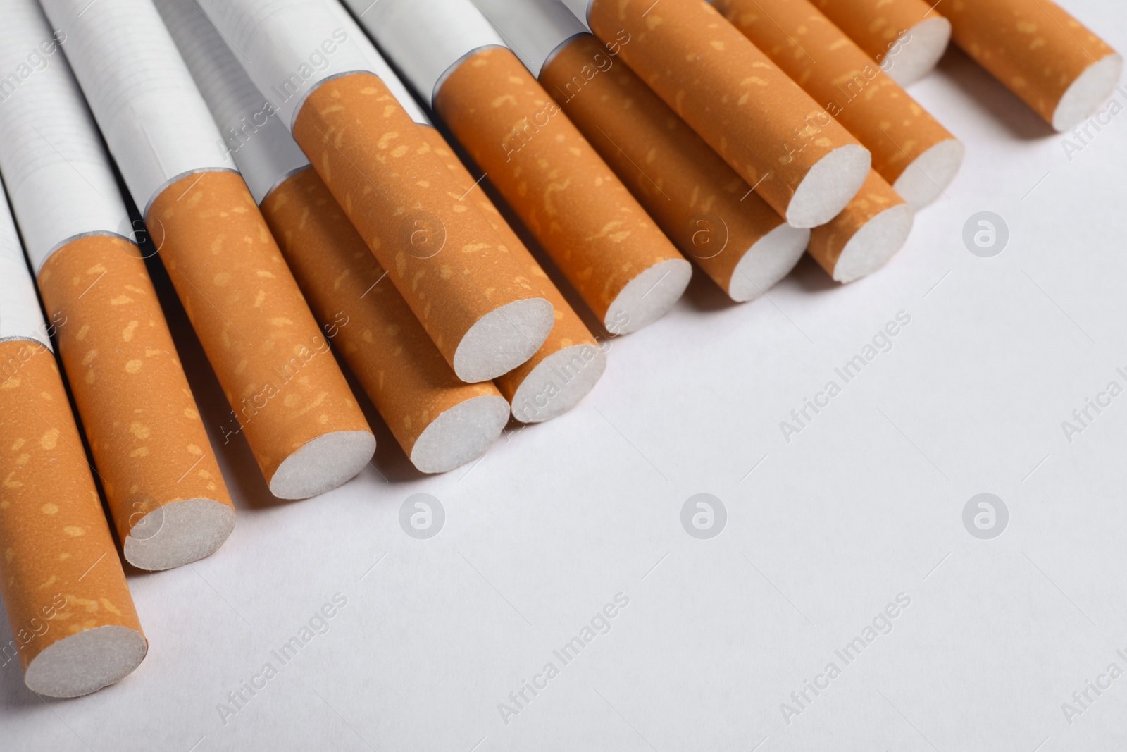 Photo of Pile of cigarettes with orange filters on white background, closeup. Space for text