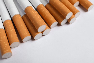 Photo of Pile of cigarettes with orange filters on white background, closeup. Space for text