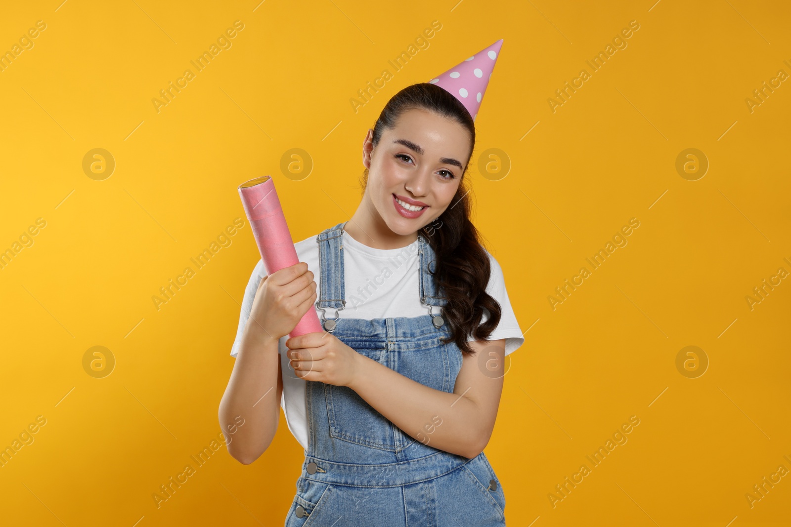 Photo of Young woman blowing up party popper on yellow background