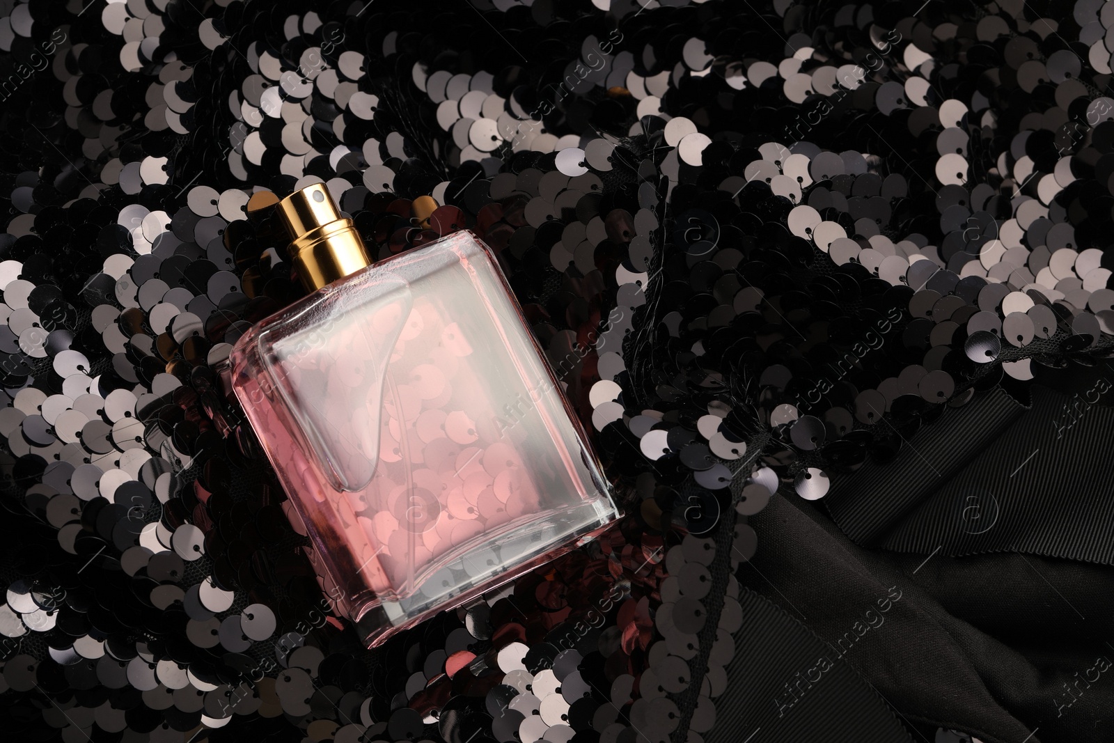 Photo of Luxury perfume in bottle on fabric with shiny sequins, above view