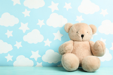 Photo of Teddy bear on wooden table near wall with painted blue sky, space for text. Baby room interior