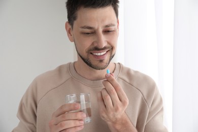 Photo of Man with glass of water taking pill at home