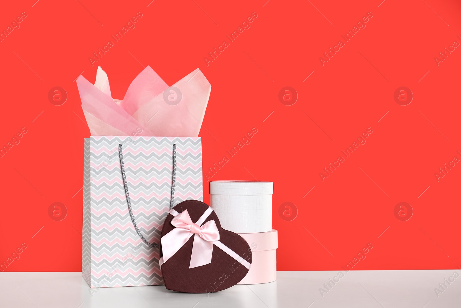 Photo of Shopping paper bag and gift boxes on red background. Space for text