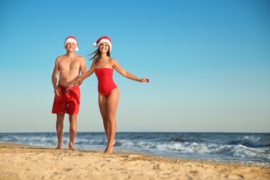 Happy couple with Santa hats together on beach. Christmas vacation