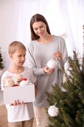 Happy mother with her cute son decorating Christmas tree together at home