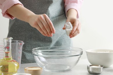 Woman adding pinch of salt into bowl at grey marble table indoors, closeup. Cooking traditional grissini