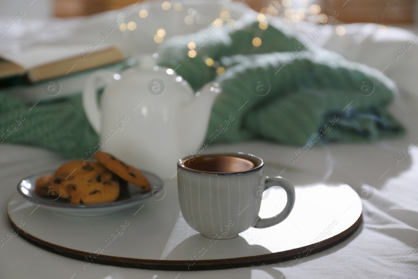 Photo of Tray with cup of hot tea, cookies and teapot on bed indoors