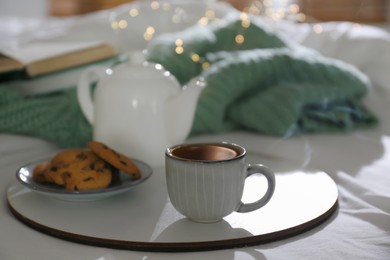 Photo of Tray with cup of hot tea, cookies and teapot on bed indoors