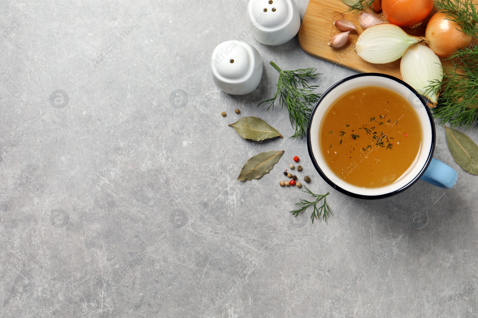 Photo of Hot delicious bouillon in cup and ingredients on light grey table, flat lay. Space for text