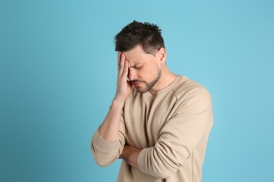 Photo of Man suffering from terrible migraine on light blue background