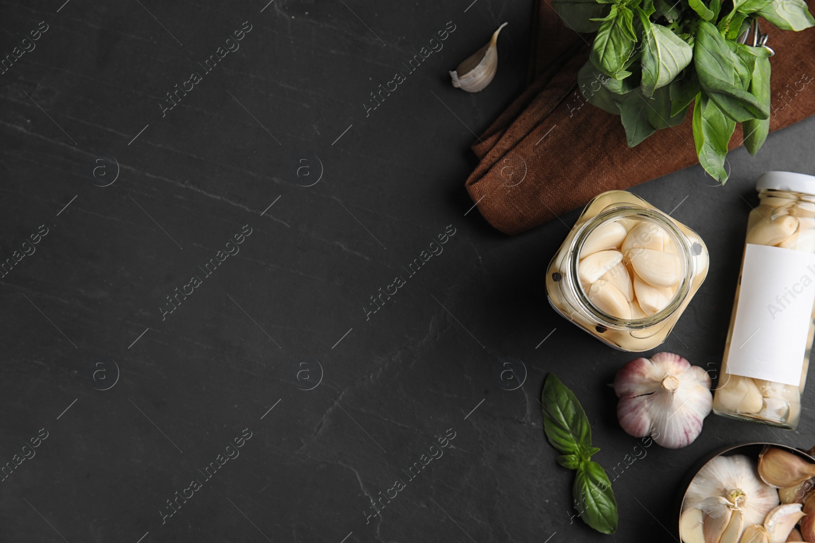 Photo of Flat lay composition with jars of pickled garlic on dark table. Space for text