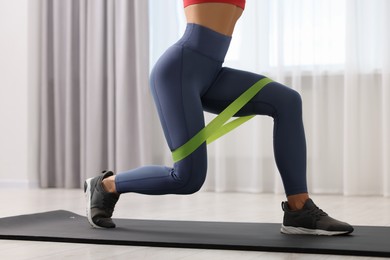Photo of Woman doing exercise with fitness elastic band on mat indoors, closeup