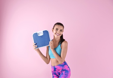 Photo of Happy young woman with scales on color background. Weight loss motivation