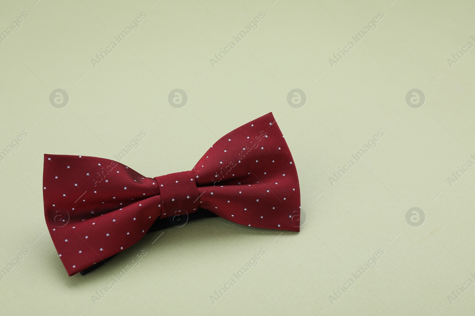 Photo of Stylish burgundy bow tie with polka dot pattern on pale green background, space for text