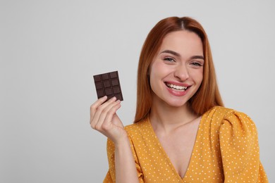 Photo of Young woman with tasty chocolate on light grey background, space for text