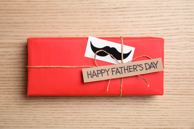 Photo of Gift box with mustache and words HAPPY FATHER'S DAY on wooden background, top view
