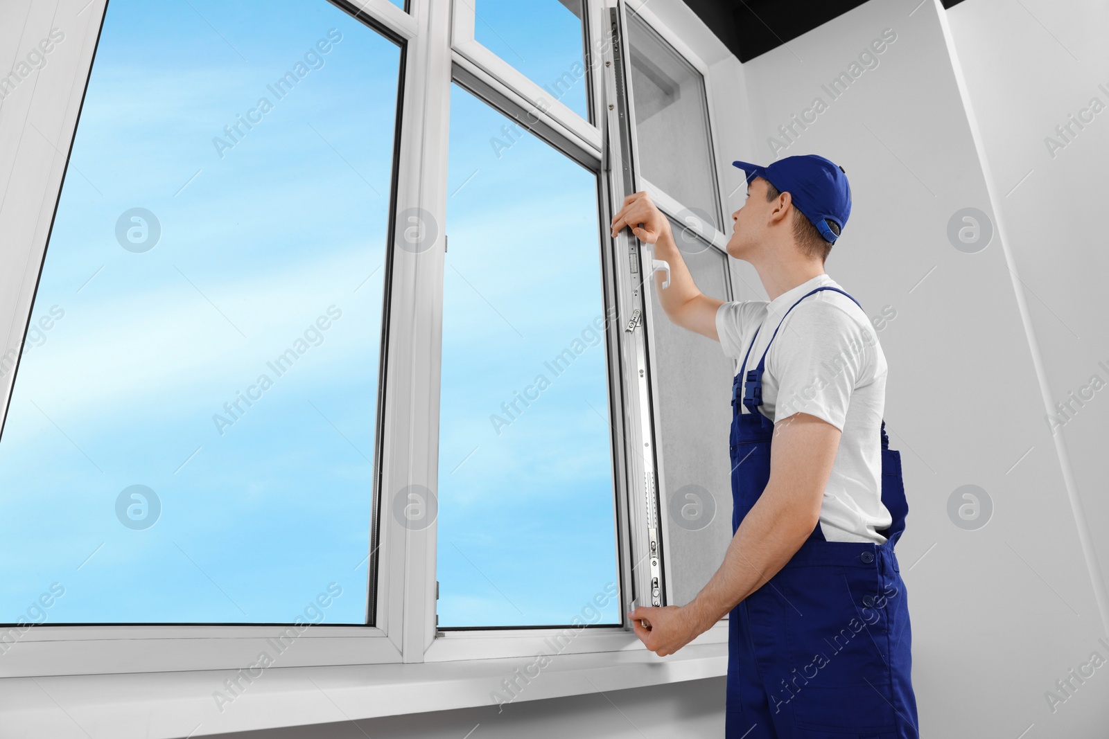 Photo of Worker in uniform installing plastic window indoors