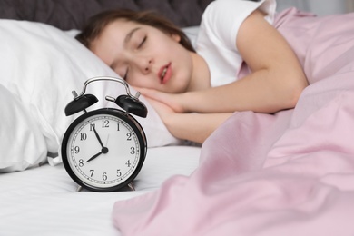 Beautiful little girl with alarm clock sleeping in bed