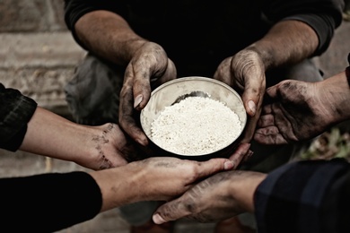 Photo of Poor homeless people with bowl of rice outdoors, closeup