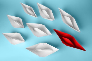 Group of paper boats following red one on light blue background, flat lay. Leadership concept