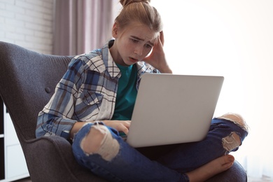 Shocked teenage girl with laptop indoors. Danger of internet