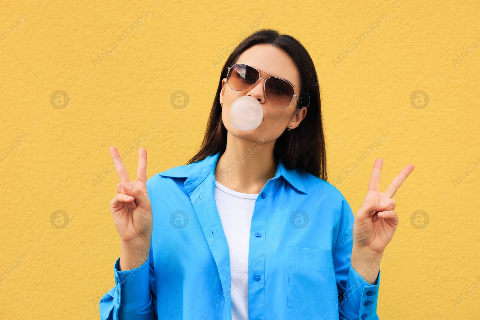 Photo of Beautiful young woman with sunglasses blowing chewing gum near orange wall