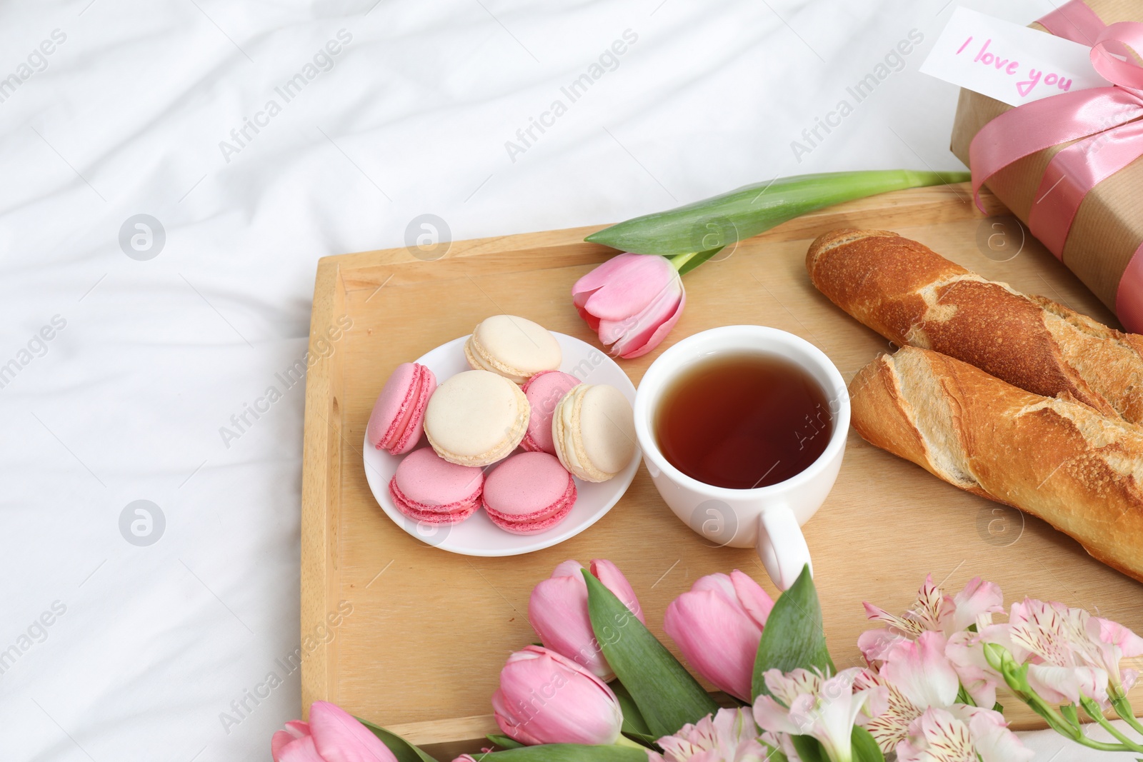 Photo of Delicious breakfast, flowers, gift box and card with phrase I Love You on bed