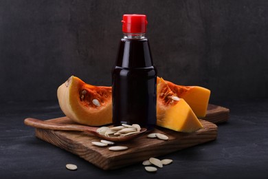 Photo of Fresh pumpkin seed oil in glass bottle on dark grey table