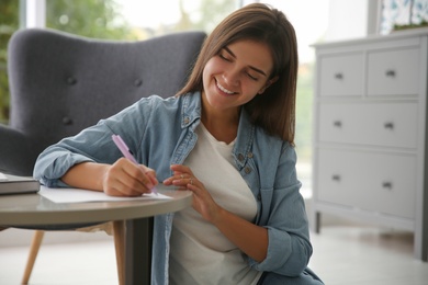 Photo of Woman writing paper letter at table indoors