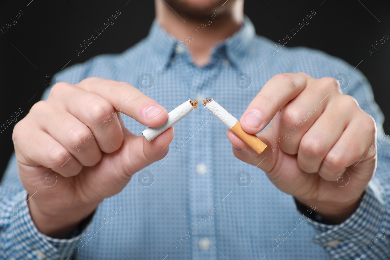 Photo of Stop smoking concept. Man holding pieces of broken cigarette on black background, closeup