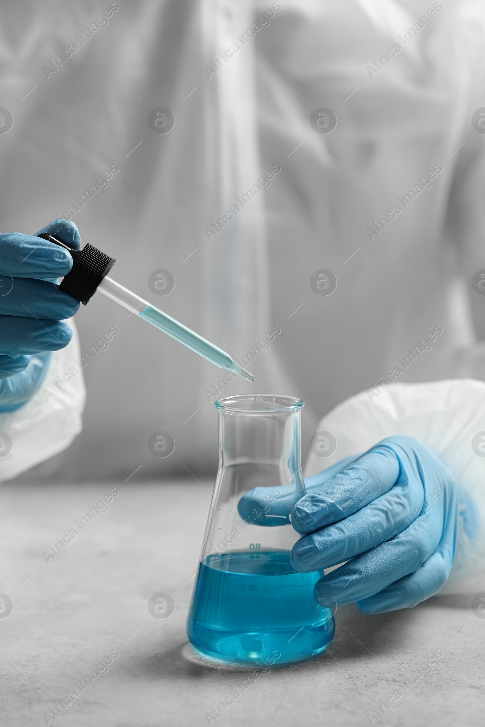 Photo of Scientist dripping liquid from pipette into beaker at white table, closeup