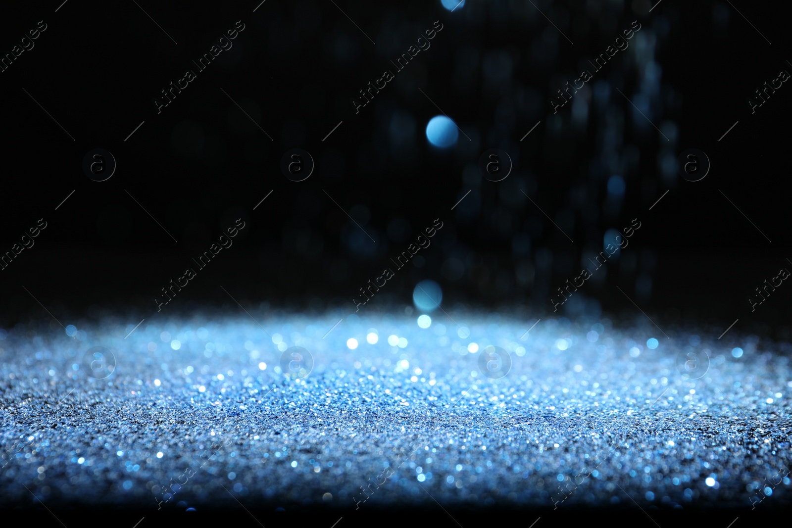 Photo of Shiny blue glitter falling down on black background. Bokeh effect
